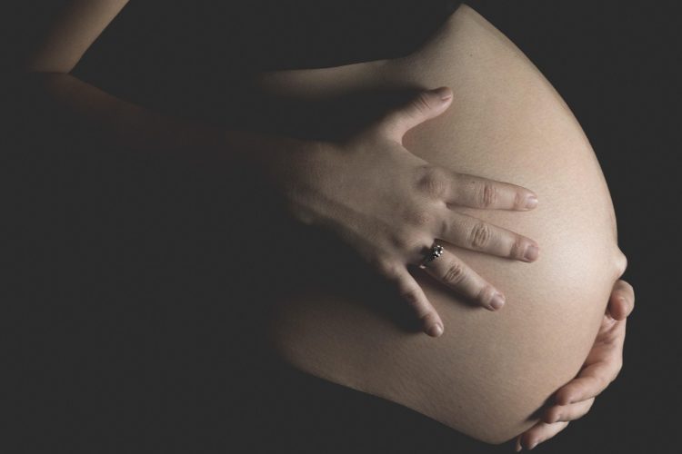 Kobieta w ciąży trzyma dłoń na brzuchu w ciemnym pomieszczeniu