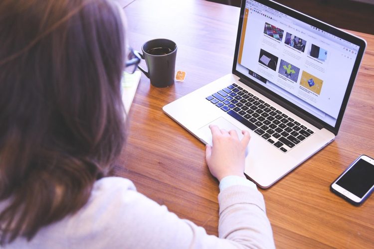 Kobieta pracująca przy laptopie siedząc przy biurku z filiżanką kawy
